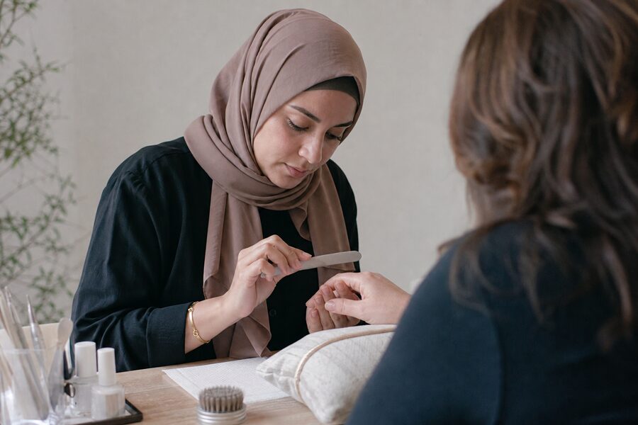 A nail artist shaping a client’s nails at her table